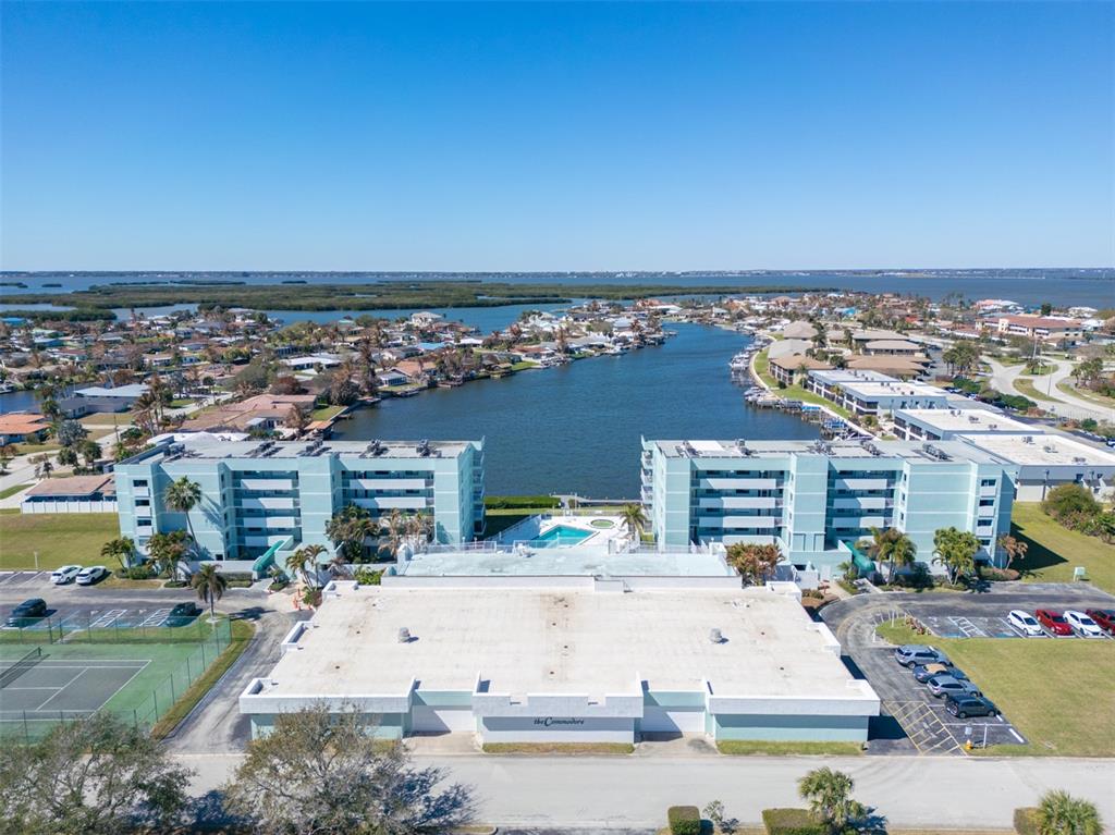 An aerial view shows a multi-story apartment complex with a pool and tennis court — 1750 COMMODORE BOULEVARD UNIT 2303, COCOA BEACH, FL