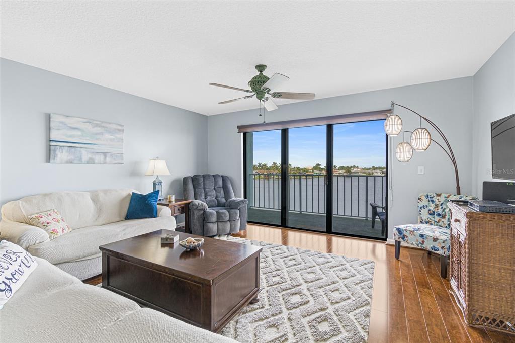 A living room features a sofa, recliner, patterned rug, and sliding glass doors overlooking water — 1750 COMMODORE BOULEVARD UNIT 2303, COCOA BEACH, FL