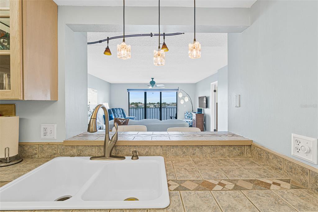 A kitchen sink with a tiled countertop overlooks a living area with a water view — 1750 COMMODORE BOULEVARD UNIT 2303, COCOA BEACH, FL