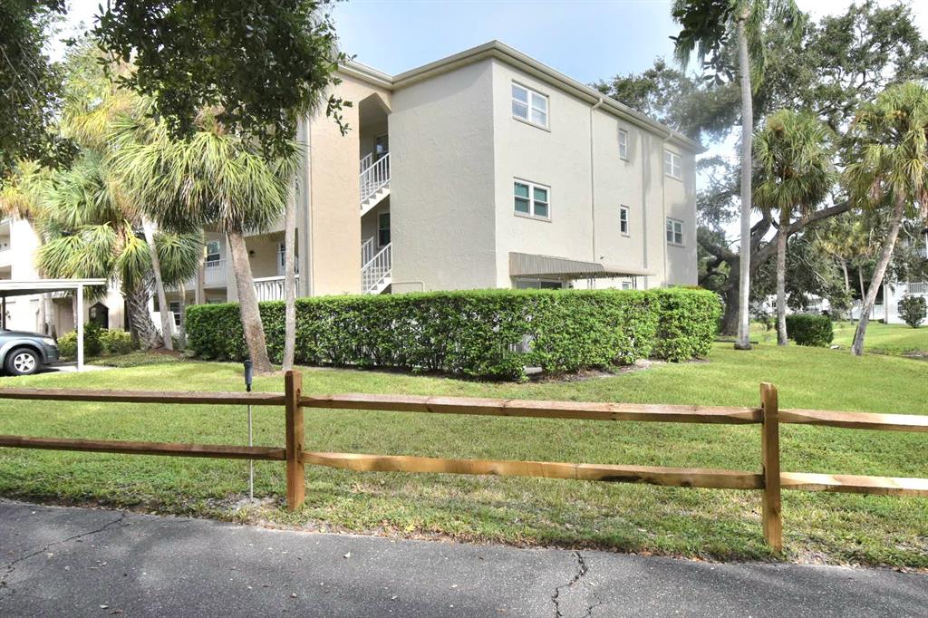 A three-story apartment building stands behind a wooden fence and a manicured lawn — 940 VIRGINIA STREET UNIT 108, DUNEDIN, FL