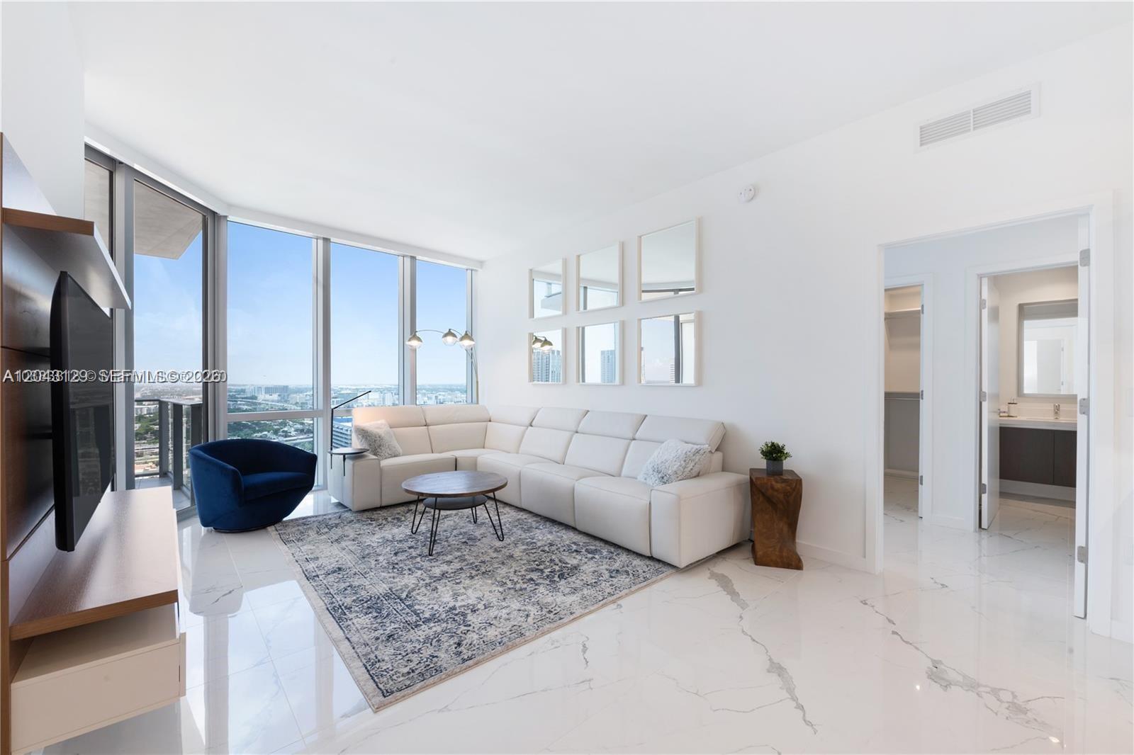 A modern living room features a white sectional sofa, blue armchair, and floor-to-ceiling windows — 851 NE 1st Ave # 3308, Miami FL 33132, MIAMI, FL