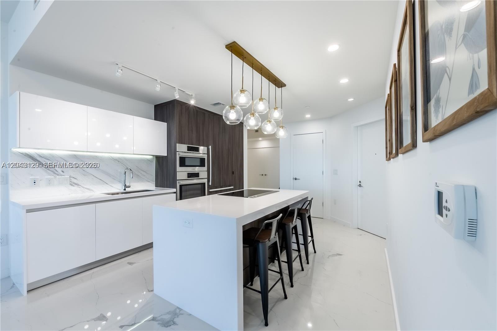 A modern kitchen features white cabinetry, a marble backsplash, and a central island with seating — 851 NE 1st Ave # 3308, Miami FL 33132, MIAMI, FL