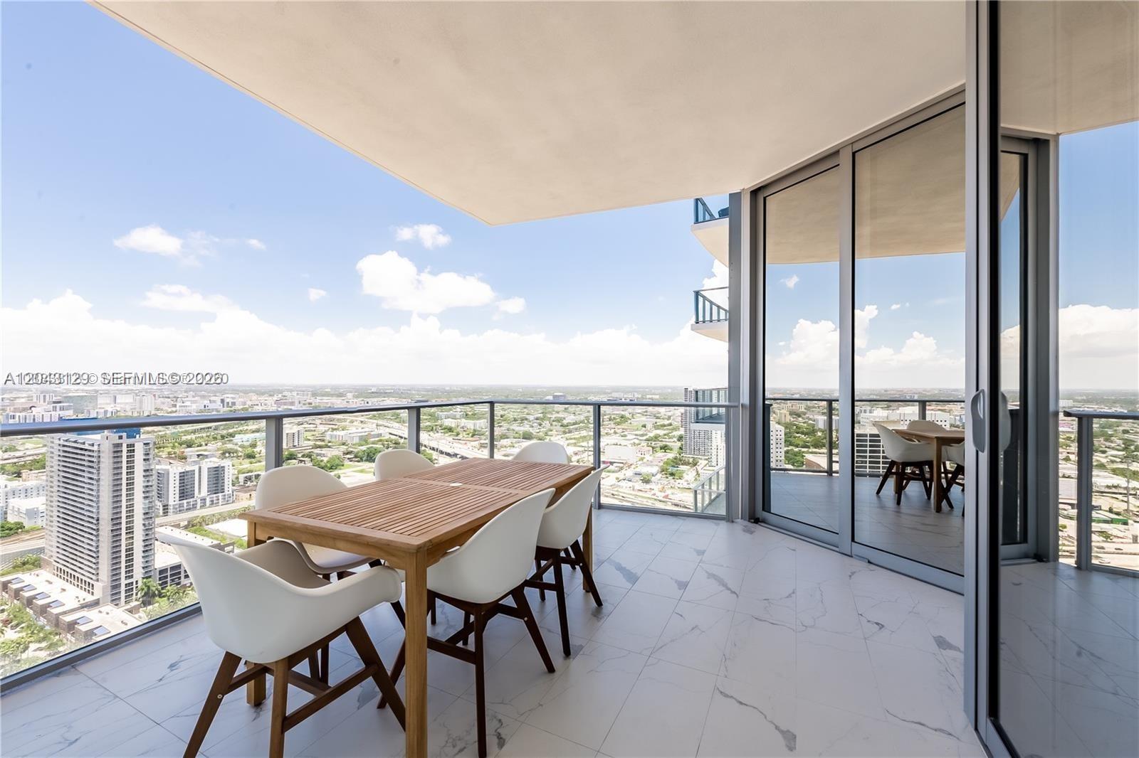 A high-rise balcony features a wooden dining set on white marble tile flooring — 851 NE 1st Ave # 3308, Miami FL 33132, MIAMI, FL