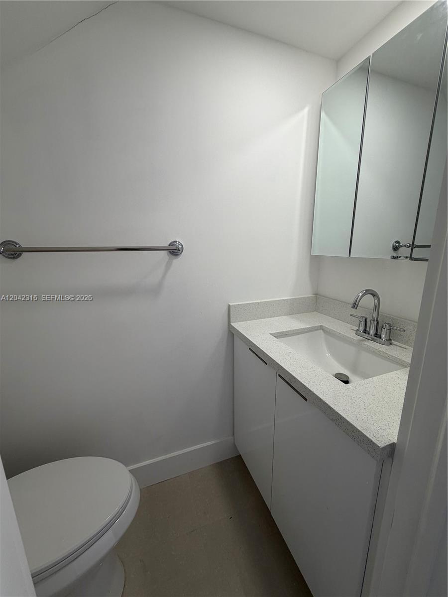 A small bathroom features a white vanity with a speckled countertop, toilet, and wall mirror — 1551 W Okeechobee Rd # 9, Hialeah FL 33010, HIALEAH, FL