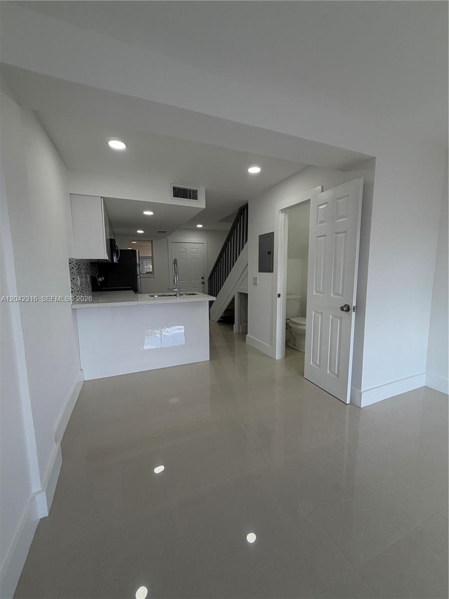 A kitchen with a breakfast bar, white cabinets, and an adjacent bathroom with stairs — 1551 W Okeechobee Rd # 9, Hialeah FL 33010, HIALEAH, FL