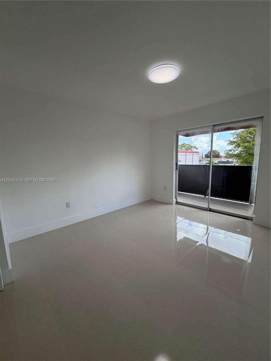 An empty room features white walls, light-colored tile flooring, a ceiling light, and a sliding glass door — 1551 W Okeechobee Rd # 9, Hialeah FL 33010, HIALEAH, FL