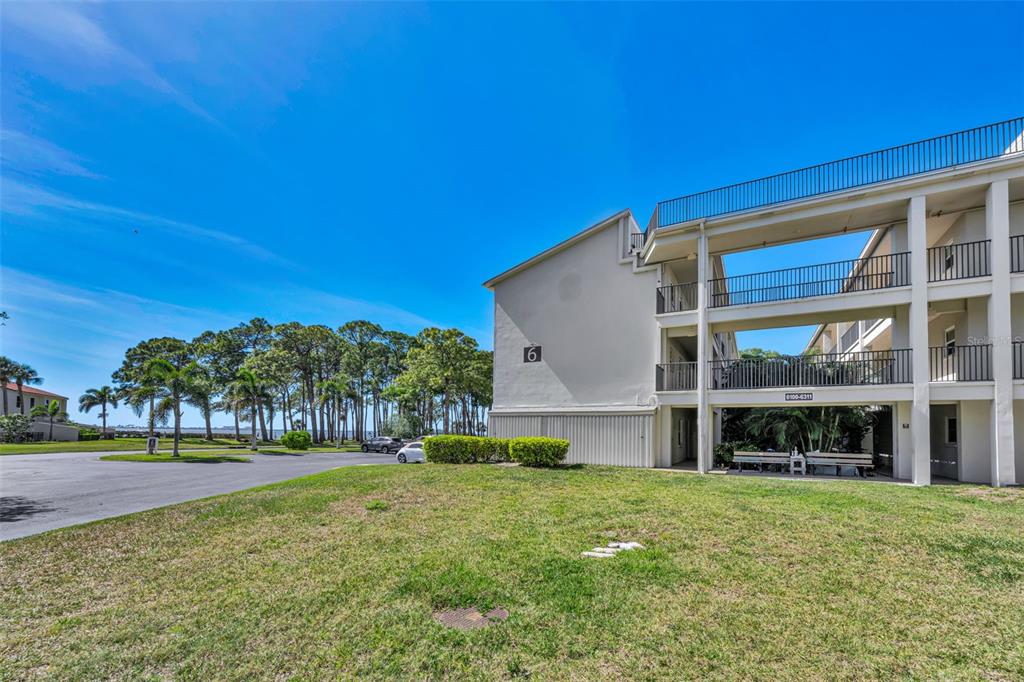 A three-story apartment building with exterior walkways stands next to a grassy lawn — 2700 BAYSHORE BOULEVARD UNIT 6107, DUNEDIN, FL
