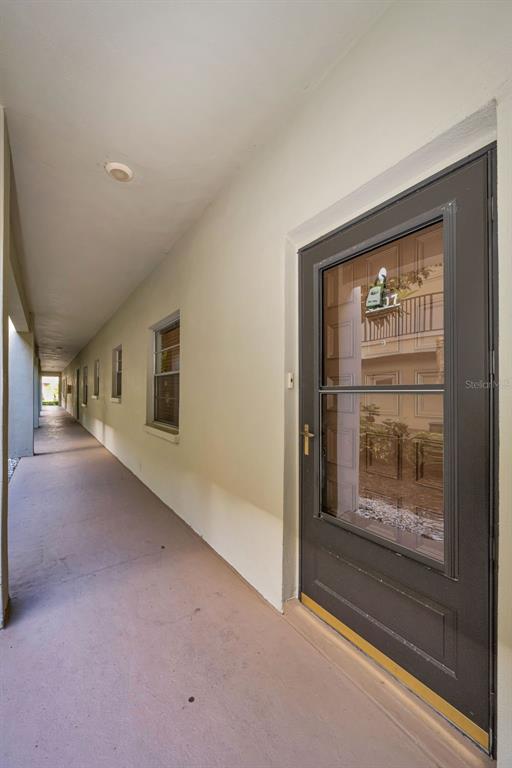 A long outdoor walkway leads past several windows to a dark gray front door — 2700 BAYSHORE BOULEVARD UNIT 6107, DUNEDIN, FL