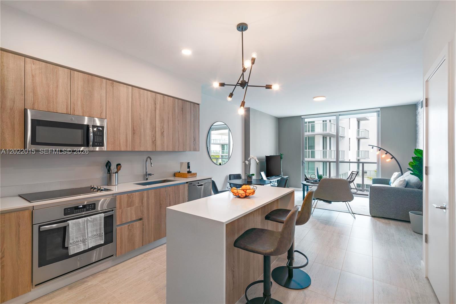 A modern kitchen with wood-grain cabinets and a white island opens to a living area — 3900 Biscayne Blvd # 818, Miami FL 33137, MIAMI, FL