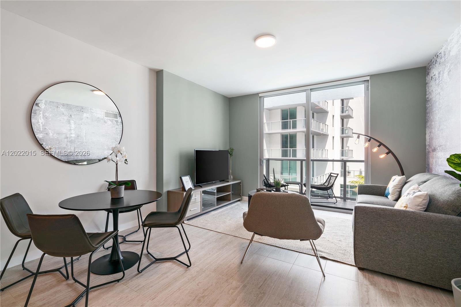 A modern living and dining area features a gray sofa, round table, and balcony access — 3900 Biscayne Blvd # 818, Miami FL 33137, MIAMI, FL