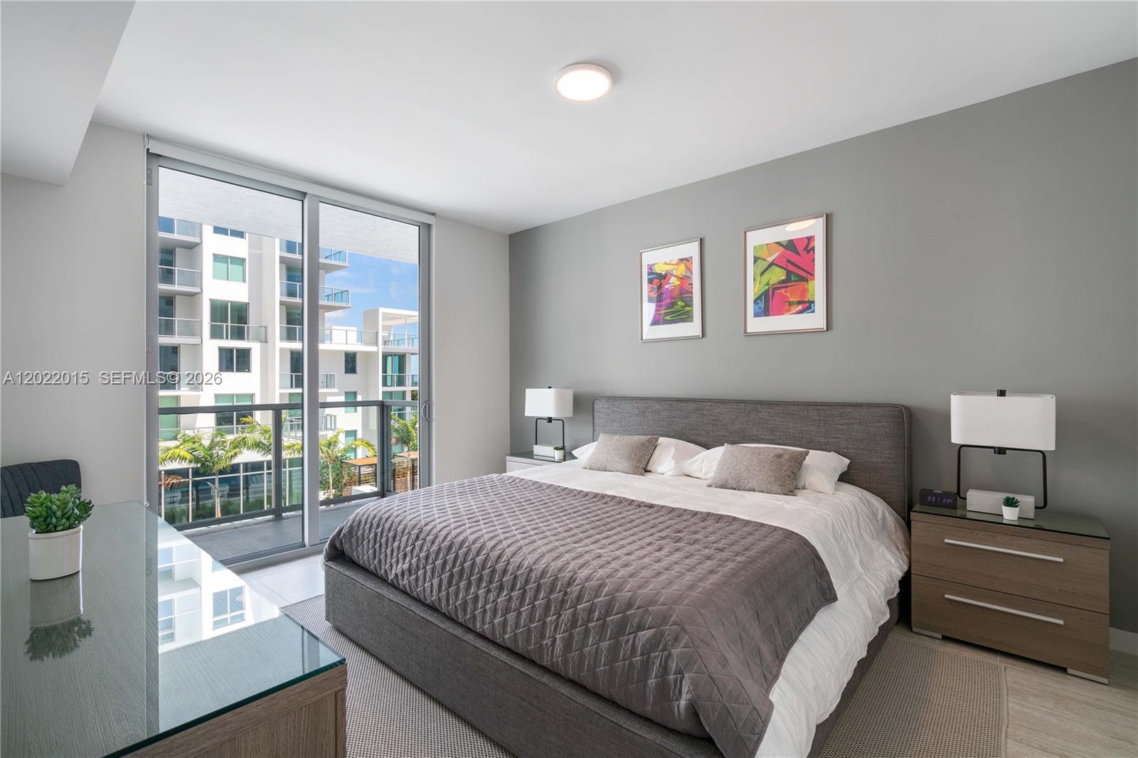 A modern bedroom features a gray upholstered bed, two nightstands, and a balcony with views — 3900 Biscayne Blvd # 818, Miami FL 33137, MIAMI, FL