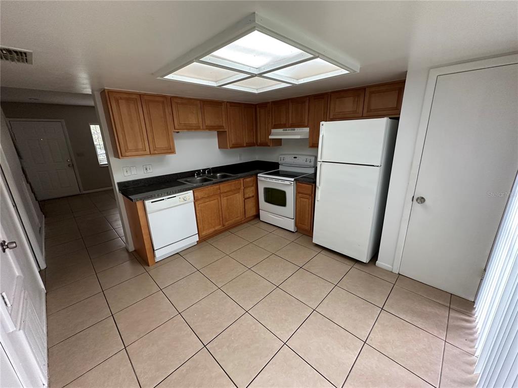 A kitchen features wood cabinets, white appliances, dark countertops, and light-colored floor tiles — 3544 KHAYYAM AVENUE, ORLANDO, FL
