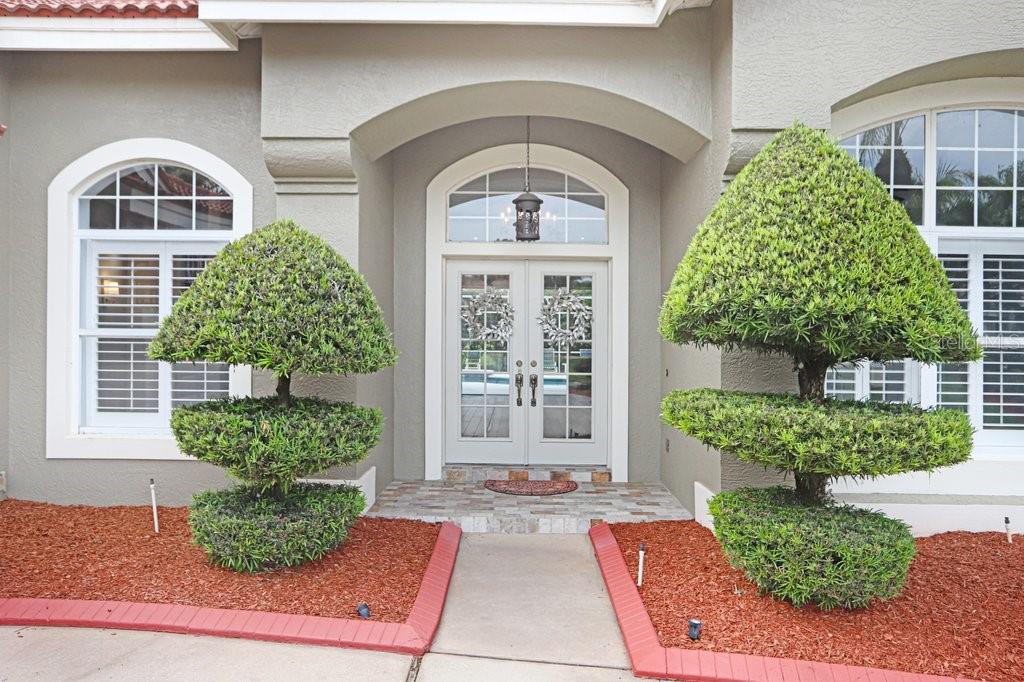 A front entrance with double glass doors, two tiered topiaries, and red mulch garden beds — 30303 LAURELWOOD LANE, WESLEY CHAPEL, FL