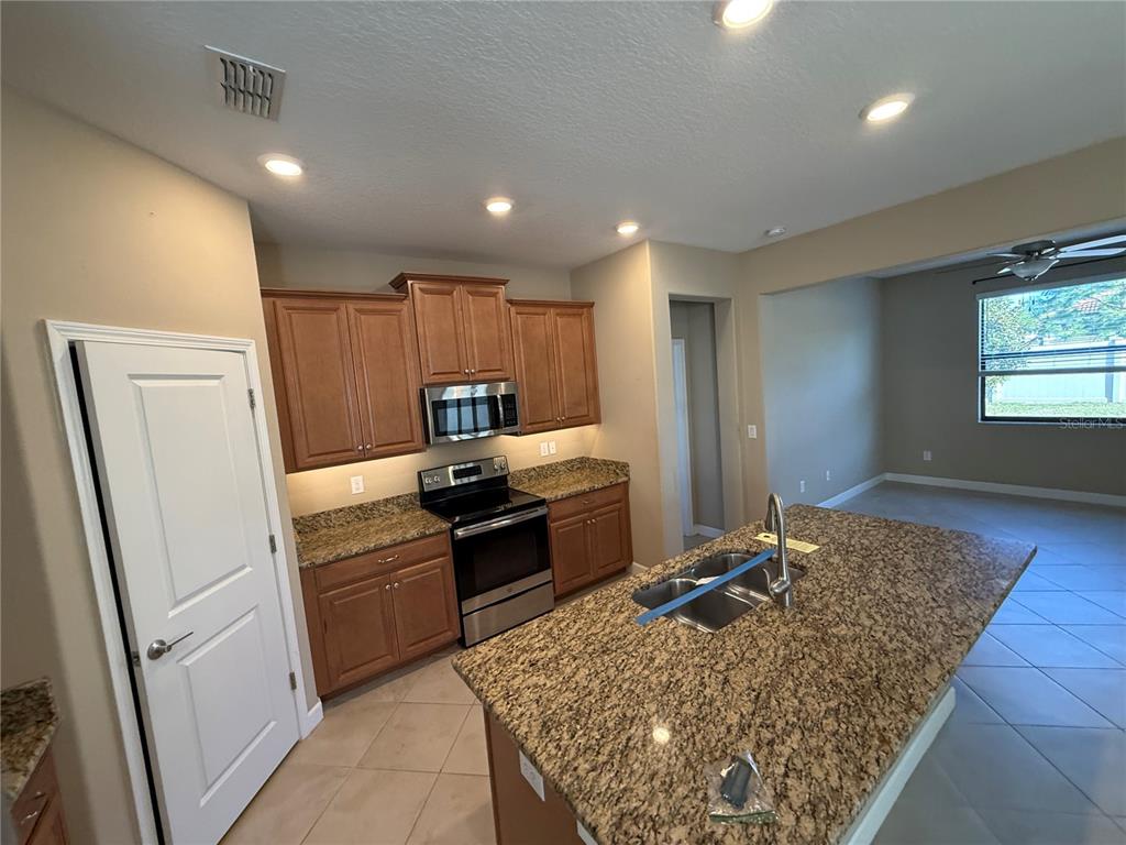 A kitchen features wood cabinets, granite countertops, a center island, and stainless steel appliances — 16852 SCUBA CREST STREET, WIMAUMA, FL