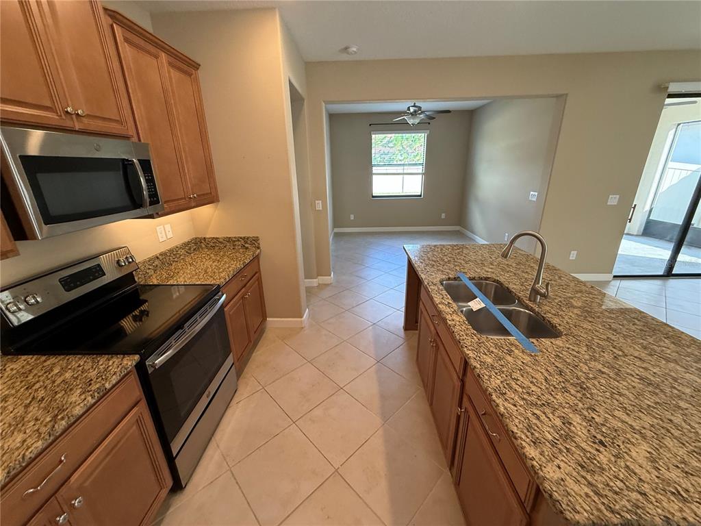 A kitchen with wood cabinets, granite countertops, stainless steel appliances, and an island sink — 16852 SCUBA CREST STREET, WIMAUMA, FL