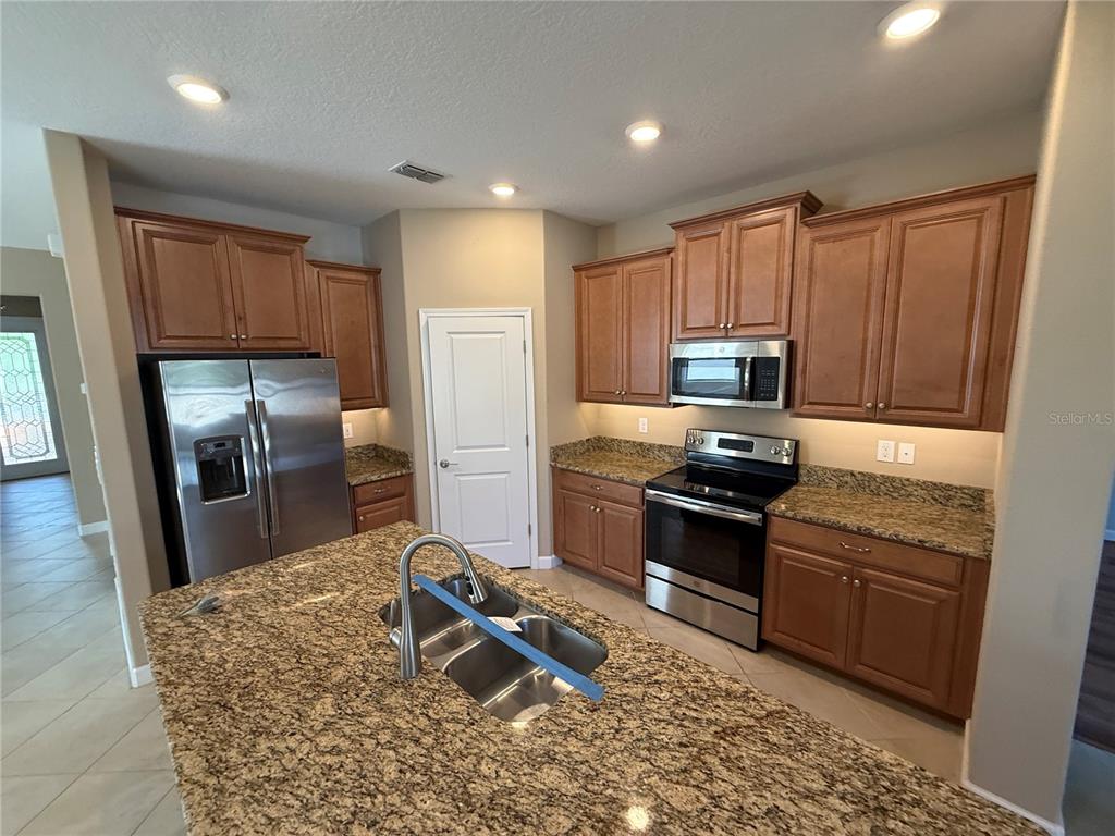A kitchen features wood cabinets, granite countertops, stainless steel appliances, and a central island sink — 16852 SCUBA CREST STREET, WIMAUMA, FL