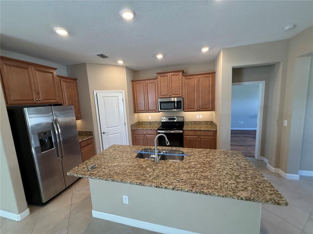 A kitchen features wood cabinets, granite countertops, stainless steel appliances, and a central island — 16852 SCUBA CREST STREET, WIMAUMA, FL