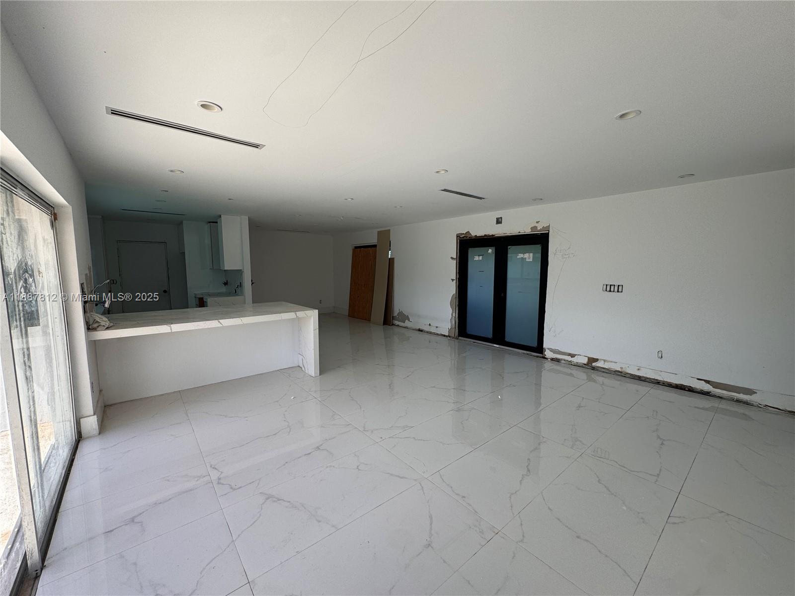 An unfinished room features white marble-look tile flooring, a kitchen island, and glass doors — 444 NW 21st St, Homestead FL 33030, HOMESTEAD, FL