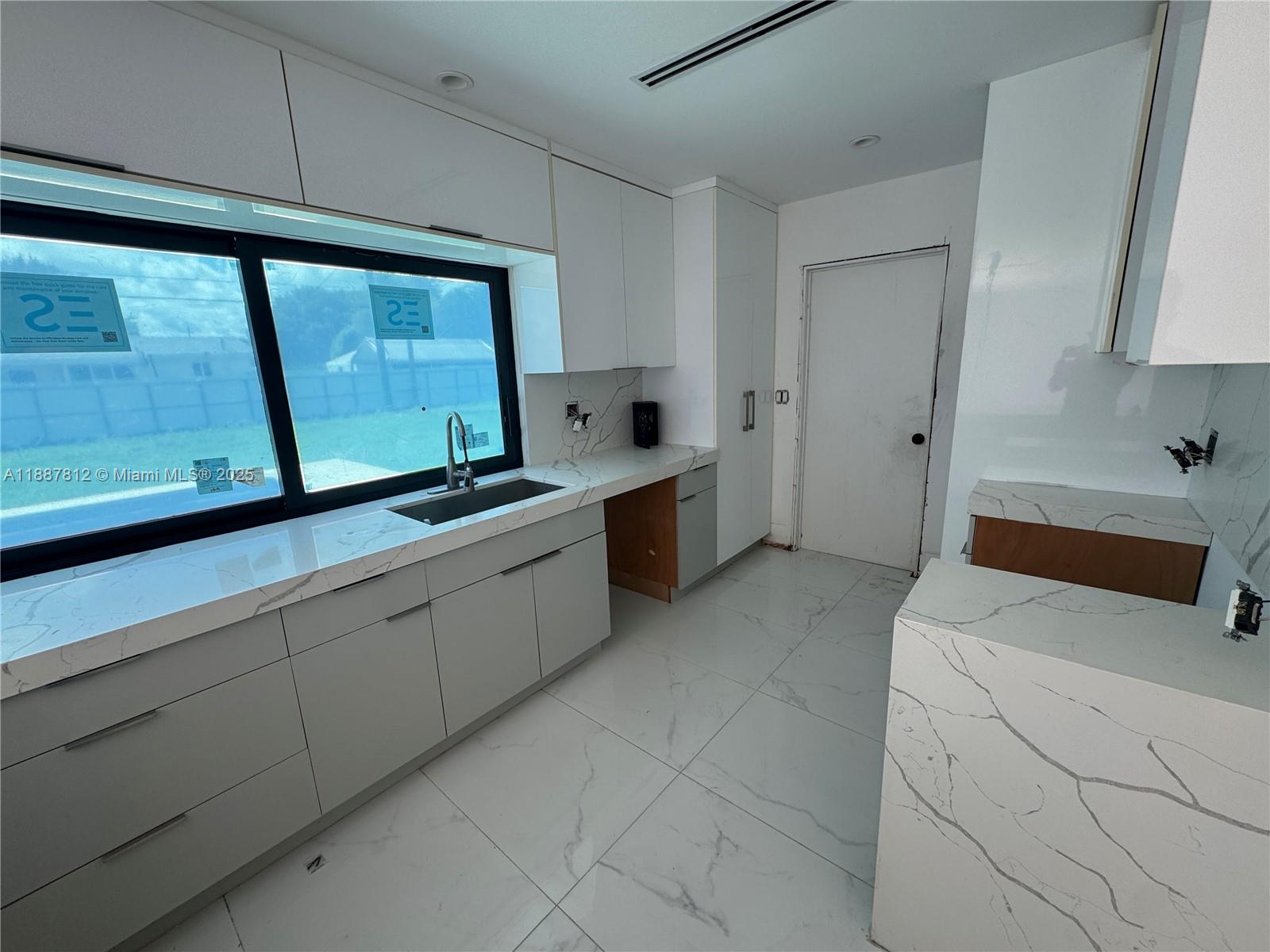 A modern kitchen features white marble countertops, light gray cabinetry, and large floor tiles — 444 NW 21st St, Homestead FL 33030, HOMESTEAD, FL