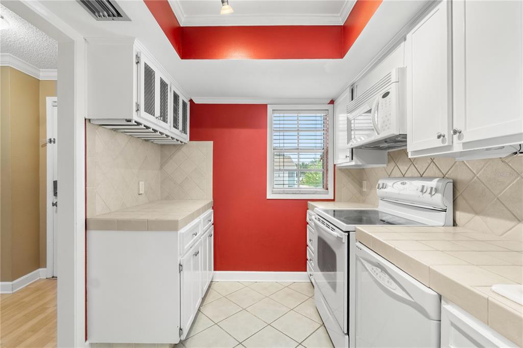 A galley kitchen features white cabinets, tile countertops, a red accent wall, and white appliances — 3823 N OAK DRIVE UNIT K22, TAMPA, FL