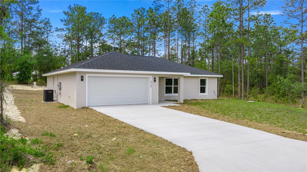 A single-story house with a white garage door and a concrete driveway sits among trees — 22433 SW RAINBOW LAKES BOULEVARD, DUNNELLON, FL