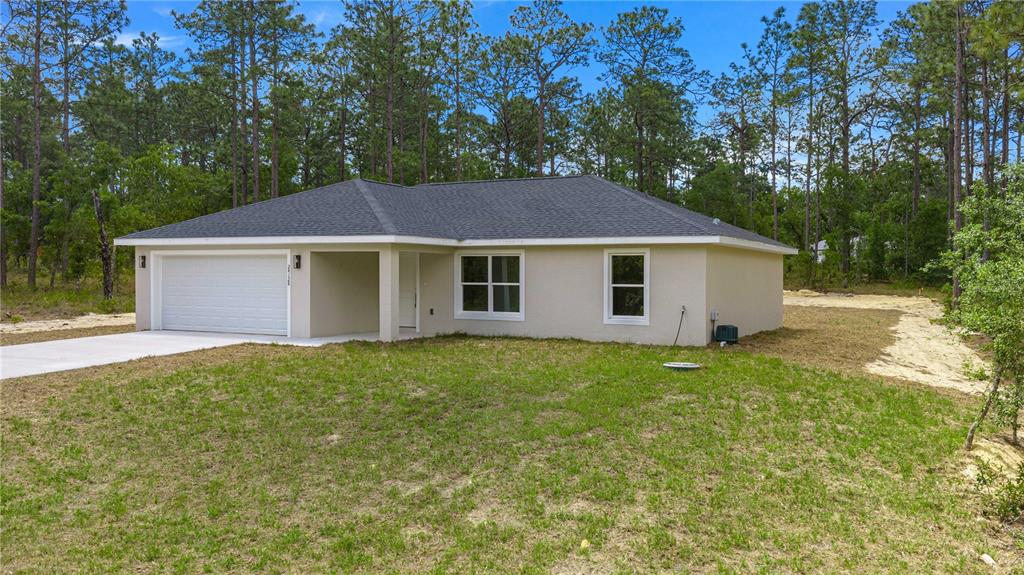 A single-story house with a two-car garage sits on a grassy lot near trees — 22433 SW RAINBOW LAKES BOULEVARD, DUNNELLON, FL