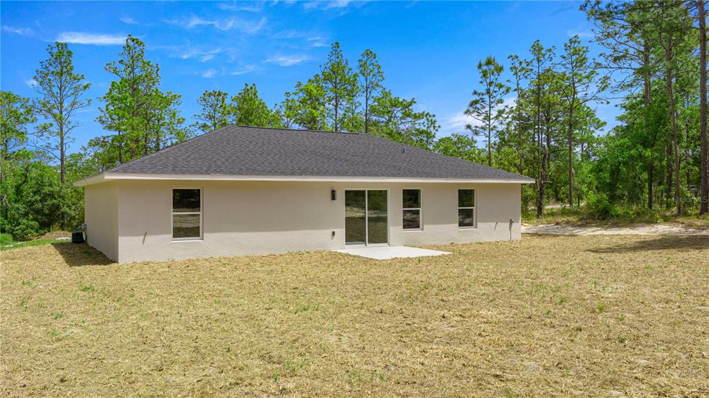 The rear exterior of a single-story beige house with a dark shingled roof and yard — 22433 SW RAINBOW LAKES BOULEVARD, DUNNELLON, FL