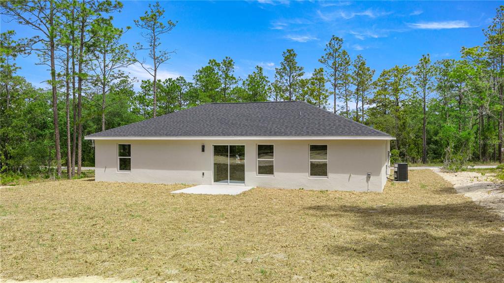 The rear exterior of a single-story beige house with a dark shingled roof and yard — 22433 SW RAINBOW LAKES BOULEVARD, DUNNELLON, FL