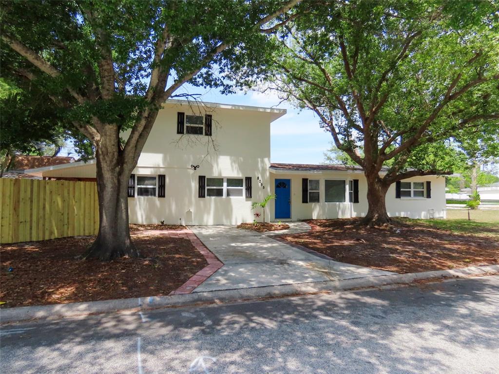 A two-story house with a blue front door, white stucco exterior, and large shade trees — 8055 33RD AVENUE N, ST PETERSBURG, FL