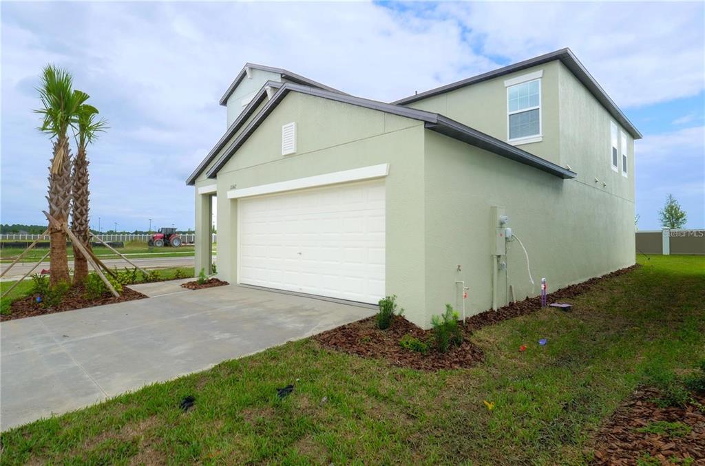 A light green two-story house with a white garage door and a concrete driveway — 11142 RADIANT SHORE LOOP, SAN ANTONIO, FL