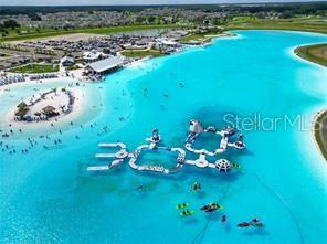 An aerial view shows a large turquoise lagoon with a floating obstacle course and beach — 11142 RADIANT SHORE LOOP, SAN ANTONIO, FL