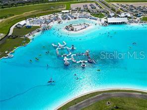 An aerial view shows a large, bright blue swimming lagoon with an inflatable obstacle course — 11142 RADIANT SHORE LOOP, SAN ANTONIO, FL