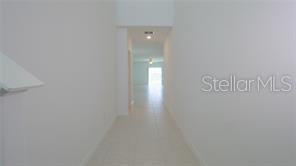 A view down a long, white-walled hallway with tile flooring leading toward a bright room — 11142 RADIANT SHORE LOOP, SAN ANTONIO, FL