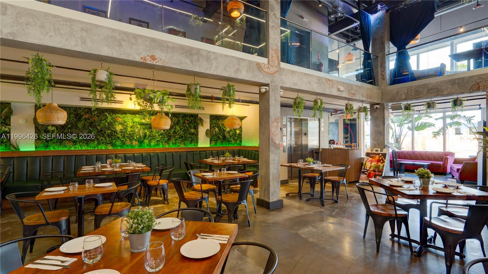 A modern restaurant interior features wooden tables, green booth seating, hanging plants, and concrete columns — Restaurant for Sale, Miami FL 33135, MIAMI, FL