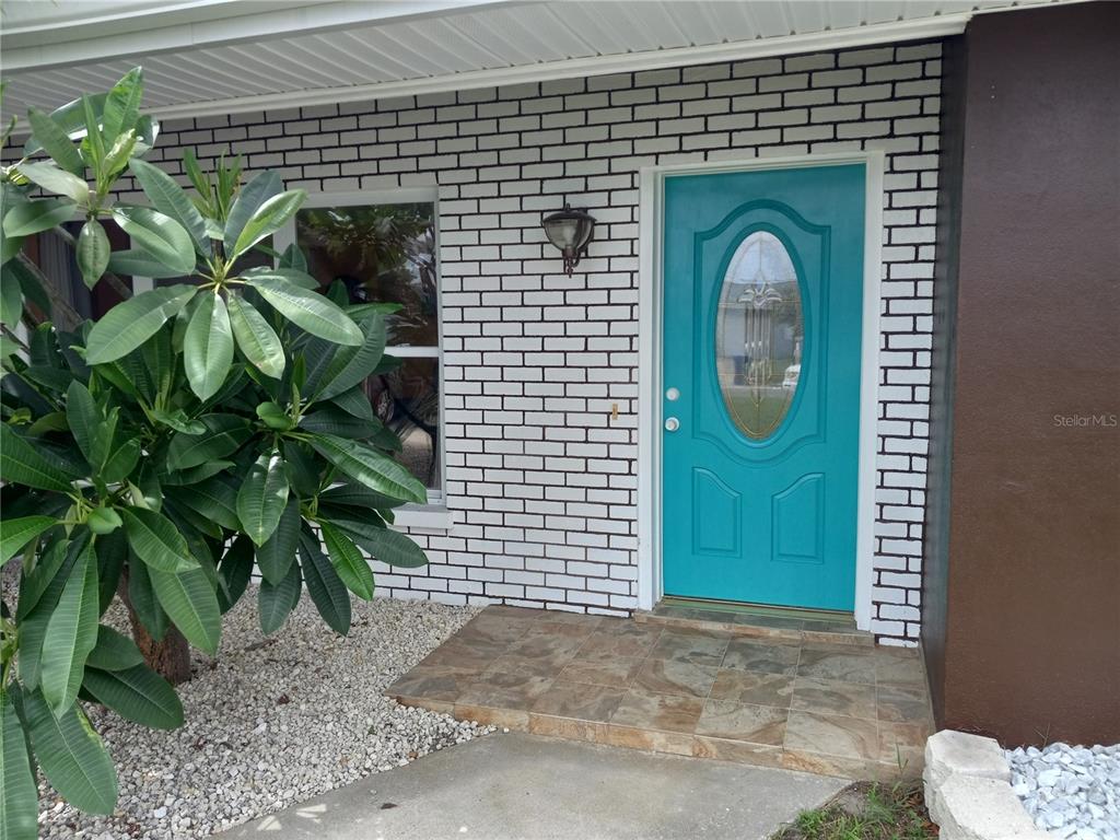 A teal front door with an oval glass insert sits beside a white brick wall — 240 REGINA DRIVE S, LARGO, FL