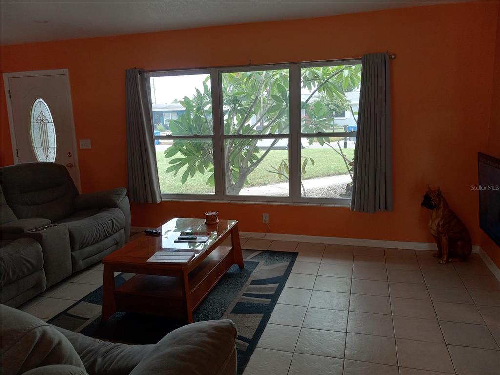 A living room with orange walls, tile flooring, a large window, and a coffee table — 240 REGINA DRIVE S, LARGO, FL