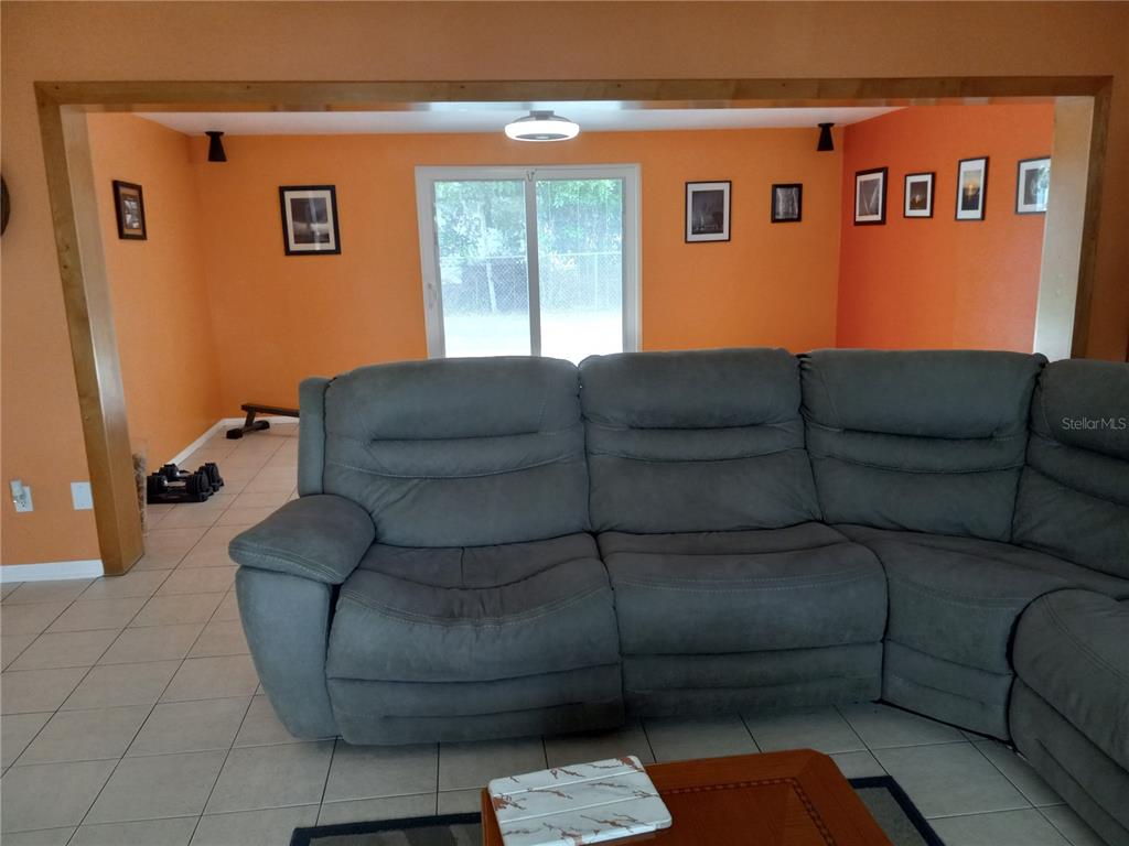 A living room with orange walls, tile floors, and a large gray sectional sofa — 240 REGINA DRIVE S, LARGO, FL
