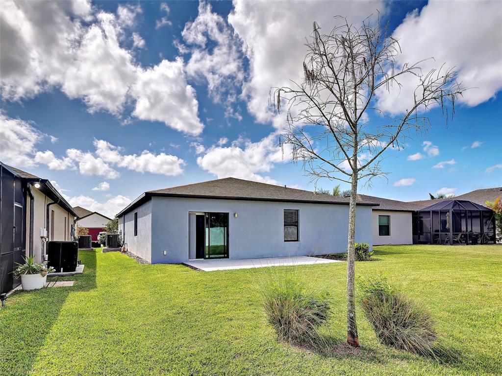 The exterior rear view of a light blue house features a concrete patio and lawn — 2065 APIAN WAY, PORT CHARLOTTE, FL