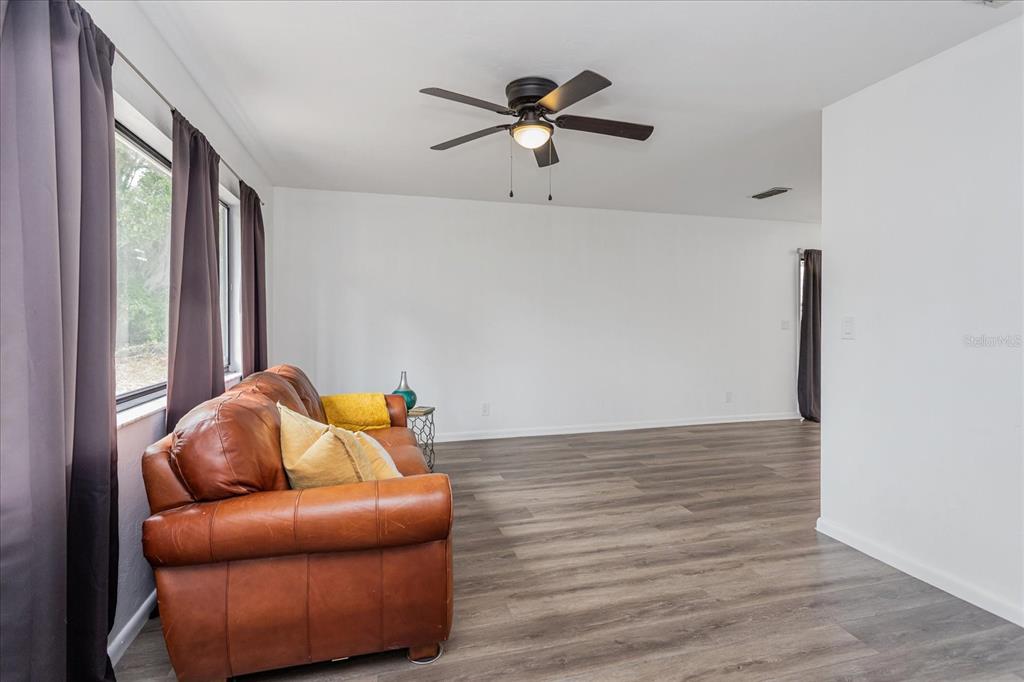 A living room features a brown leather sofa, grey wood-look flooring, and a ceiling fan — 2134 NE 45TH AVENUE, OCALA, FL
