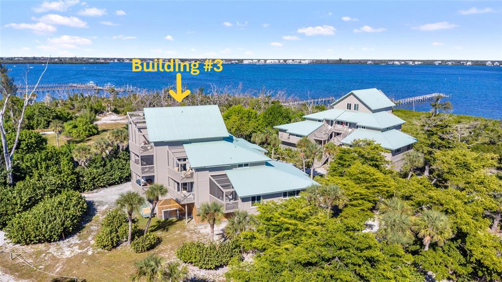 An aerial view shows two multi-story buildings with light green metal roofs near water — 9200 LITTLE GASPARILLA UNIT 304, PLACIDA, FL