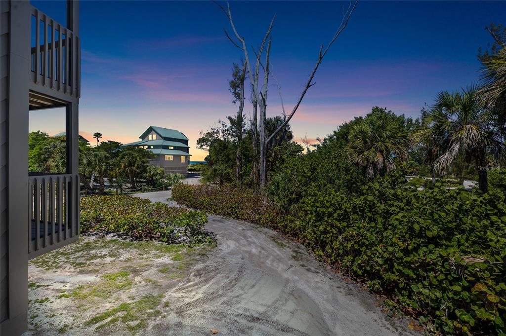 A sandy path leads through lush vegetation toward a multi-story house near the ocean — 9200 LITTLE GASPARILLA UNIT 304, PLACIDA, FL