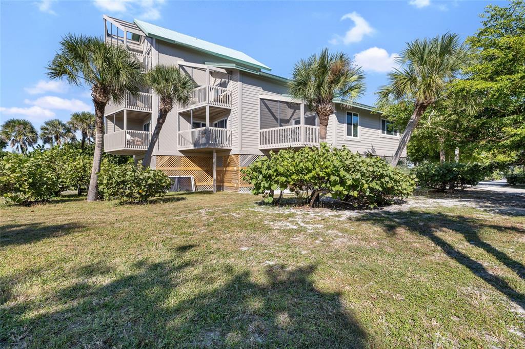 A multi-story house with balconies and a screened porch sits on a grassy, palm-filled lot — 9200 LITTLE GASPARILLA UNIT 304, PLACIDA, FL