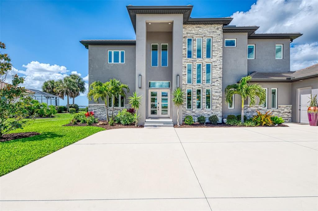 A two-story modern house with a stone facade, gray stucco, and a large concrete driveway — 3051 RIVERSHORE LANE, PORT CHARLOTTE, FL