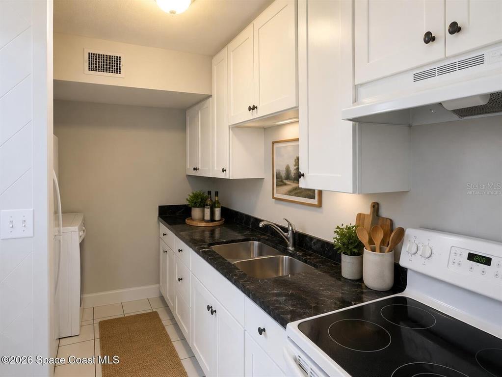 A kitchen features white cabinets, dark countertops, a double sink, and a white stove — 50 NEEDLE BOULEVARD UNIT 6, MERRITT ISLAND, FL