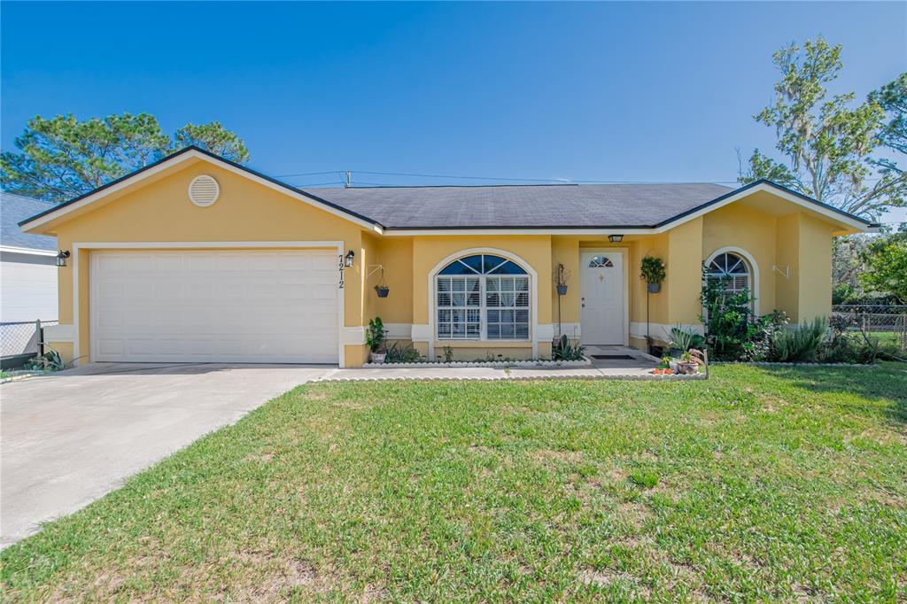 A single-story yellow house with a two-car garage, arched windows, and a front lawn — 7212 PEBBLE PASS LOOP, LAKELAND, FL