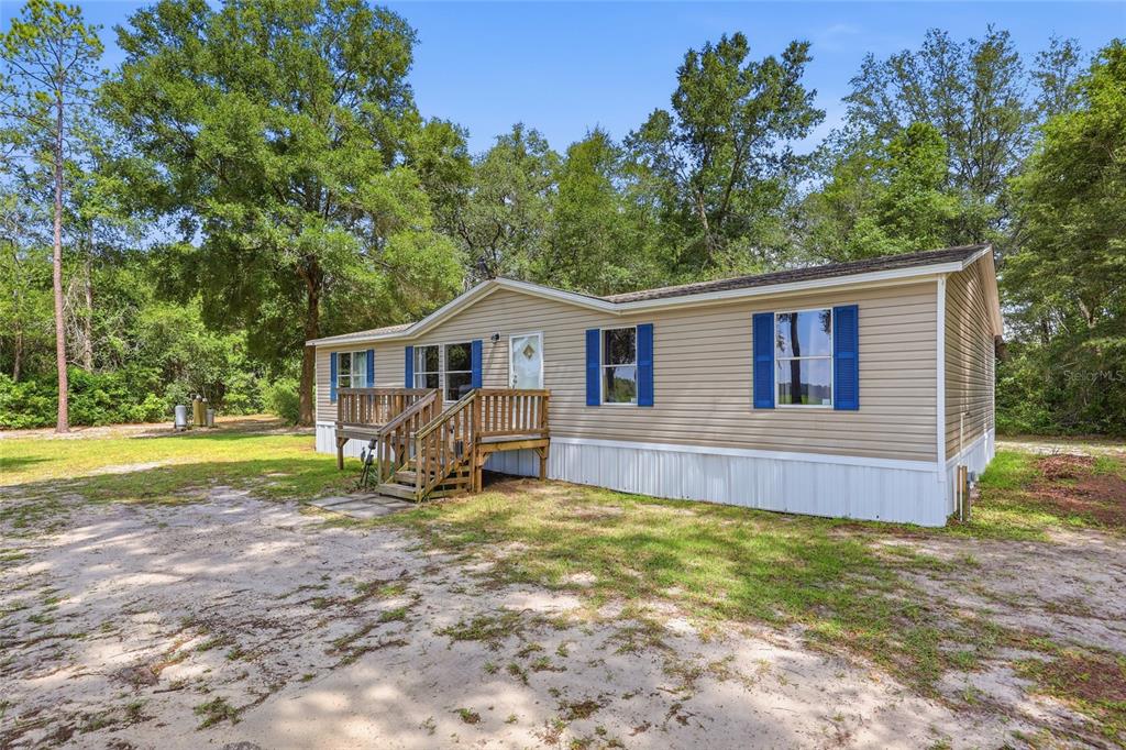 A single-story manufactured home with tan siding, blue shutters, and a wooden front deck — 3562 NW 20TH AVENUE, BELL, FL