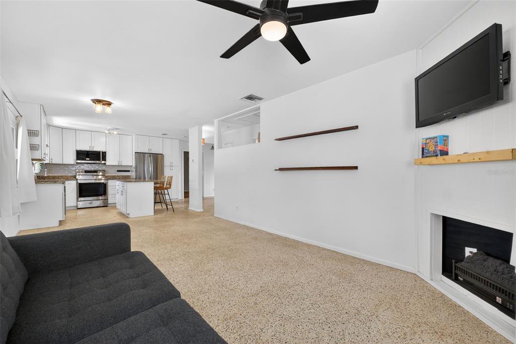 A living room with a fireplace and television opens to a white kitchen with island — 5400 97TH TERRACE N, PINELLAS PARK, FL
