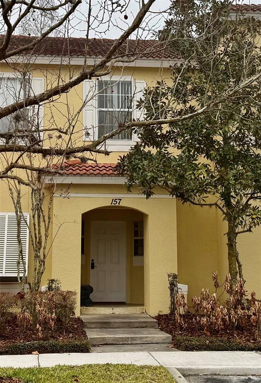 The exterior of a two-story yellow stucco townhouse features a covered entryway and white shutters — 157 POMPANO BEACH DRIVE, KISSIMMEE, FL