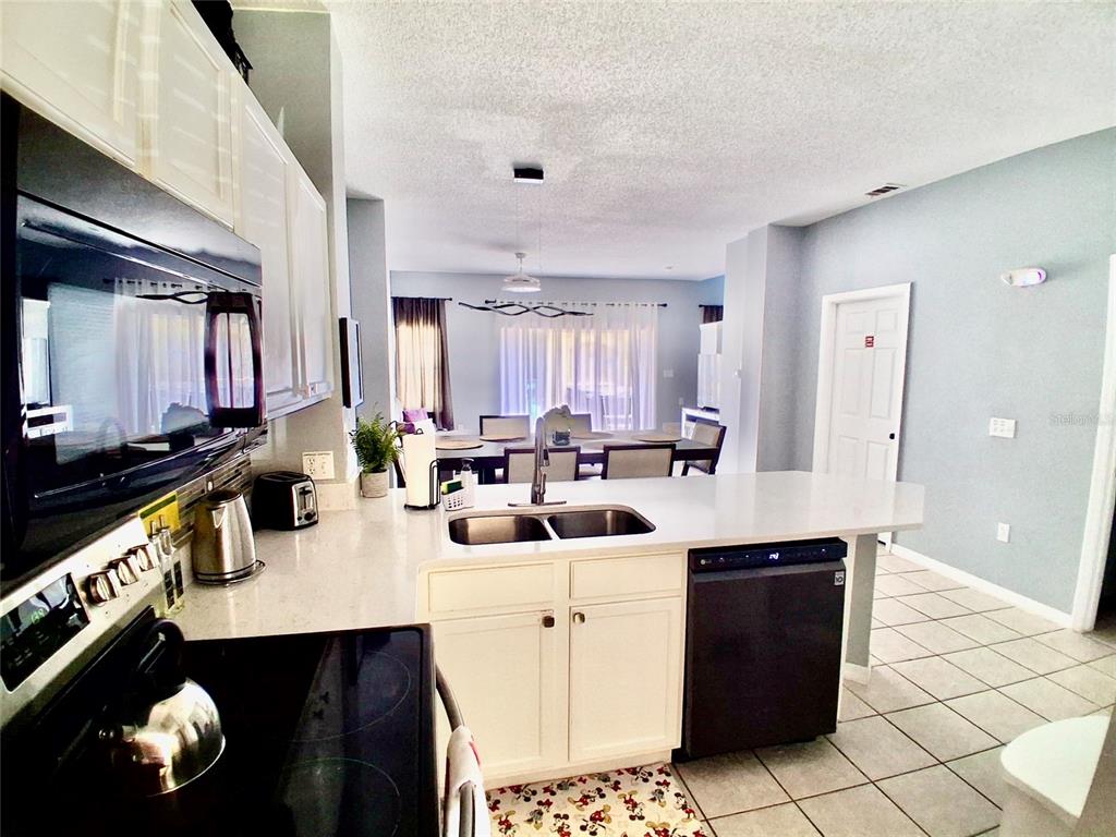 A kitchen with white cabinets, stainless steel appliances, and a breakfast bar overlooking a dining area — 157 POMPANO BEACH DRIVE, KISSIMMEE, FL