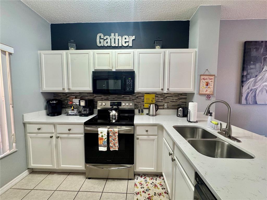 A kitchen features white cabinets, a black microwave and stove, and a light-colored countertop — 157 POMPANO BEACH DRIVE, KISSIMMEE, FL